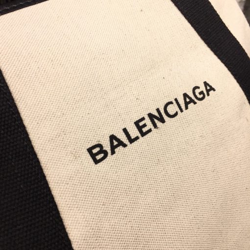 BALENCIAGA 'Cabas' Canvas and Leather Tote. Authentic Quality Bag with literature, dust bag, box and authenticity card. This Cabas tote has been made from Ecru canvas that's solely decorated with the iconic brand's updated logo lettering. Trimmed with smooth black leather at the edges and handles, it's fitted with snap fastenings at each side to create extra room on the days you need to carry your tablet or a notebook. | CRIS&COCO Authentic Quality bags and Accessories