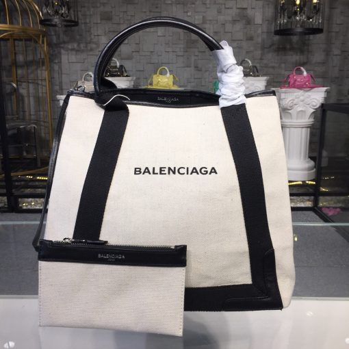 BALENCIAGA 'Cabas' Canvas and Leather Tote. Authentic Quality Bag with literature, dust bag, box and authenticity card. This Cabas tote has been made from Ecru canvas that's solely decorated with the iconic brand's updated logo lettering. Trimmed with smooth black leather at the edges and handles, it's fitted with snap fastenings at each side to create extra room on the days you need to carry your tablet or a notebook. | CRIS&COCO Authentic Quality bags and Accessories
