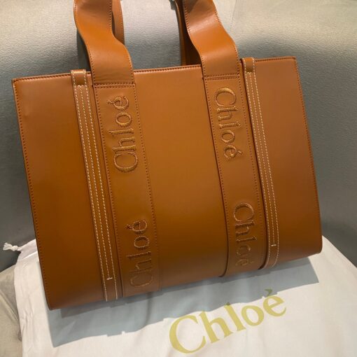 CHLOÉ Woody Tote Bag.  Original Quality Bag including gift box, care book, dust bag, authenticity card. Crafted from smooth calfskin for a natural look with a unique, luxurious feel, this Woody tote bag is a soft day-to-evening bag with a long, removable strap in addition to the top handles. The roomy inside compartment includes a practical flat pocket in leather for an elevated touch. Linen lining matches a refined finish with a lower environmental impact. The Woody line is characterised by the signature Chloé logo carried over from the Maison's iconic mules. It showcases a modern, minimalist silhouette. | CRIS&COCO Authentic Quality Designer Bag and Luxury Accessories