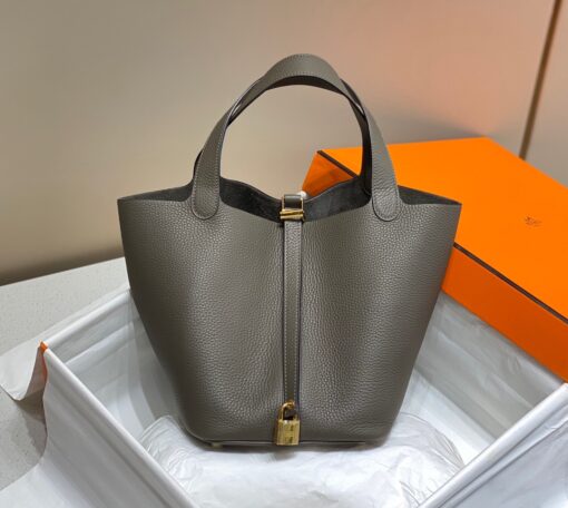 HERMÈS Picotin Lock Bag. Original Quality Bag including gift box, care book, dust bag, authenticity card. This timeless and minimalist bindle is inspired by horse feeders and is equipped with a discreet padlock. It takes its name from an old French term for the measure of oats given to a horse. The Picotin is the perfect equestrian escort, available in unlined leather that showcases the material; or in canvas and leather with outside pockets for a light, casual and functional wear. | CRIS&COCO Authentic Quality Designer Bags and Luxury Accessories