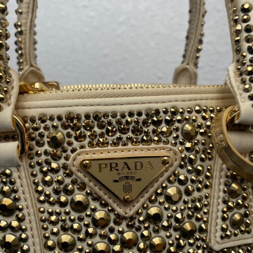 PRADA Galleria Satin Mini Bag With Crystals. Original Quality Bag including gift box, care book, dust bag, authenticity card. A surface of dazzling crystals in various sizes creates a precious play of sparkles and glimmers on this Prada Galleria bag, recalling the jewelry world. The accessory, which exemplifies the centennial excellence of Prada in luxury leather goods, becomes a reflection of the brand's modernity and stylistic identity that seeks to interpret kaleidoscopic contemporaneity through a pragmatic design and structured lines. Presented in a mini version, the bag is made of fine silk satin. The Prada Galleria bag, named after the historic Prada store opened by Mario Prada in 1913 in Galleria Vittorio Emanuele II in Milan, expresses the quintessence of the brand's timeless elegance. | CRIS&COCO Authentic Quality Designer Bags and Luxury Accessories