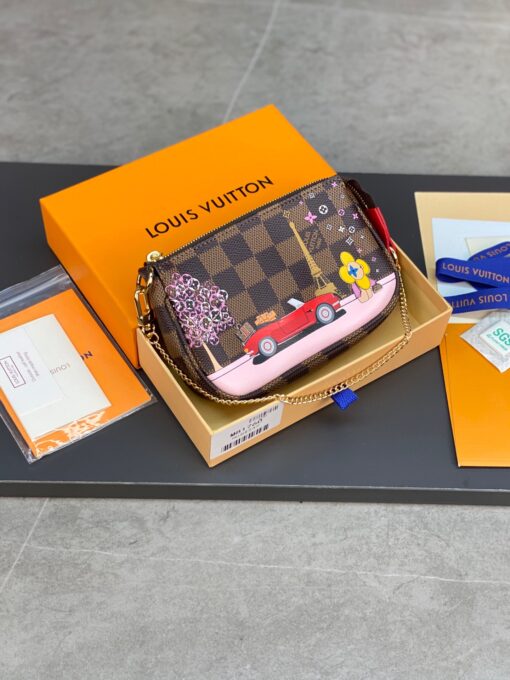LOUIS VUITTON Mini Pochette Accessoires Pouch. High-End Quality Bag including gift box, care book, dust bag, authenticity card. This pochette is crafted of traditional damier checkered toile canvas in brown. The bag features a colorful depiction of house mascot Vivienne driving by the Eiffel Tower in Paris, and a polished brass chain link wristlet strap. The top zipper opens to a compact fabric interior. This is a chic and playful pochette, with luxury and style. | CRIS AND COCO Authentic Quality Luxury Accessories
