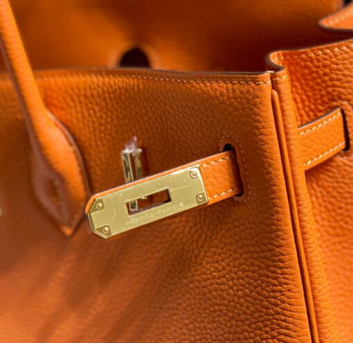 HERMÈS Birkin. Exquisite Craftsmanship and Timeless Elegance: Discover the Allure of the HERMES Birkin Bag Large Leather Top Handle. Designed with the actress Jane Birkin in mind, the Birkin bag is a contemporary development of the Kelly bag. Created based on Jane's suggestions, it was architected to be more significant to fit modern women's fast-paced life, with several minor yet outstanding adaptations, such as the elongated top handles. The French Birkin 30 bag is a classic touch of elegance to your look! The accessory features a trapeze body, a pebbled leather texture, a hanging key fob, gold-tone hardware, round top handles, a padlock fastening detail, a foldover top with twist-lock closure, a front center logo stamp, an internal zipped pocket, and purse feet. | CRIS AND COCO Authentic Quality Luxury Accessories