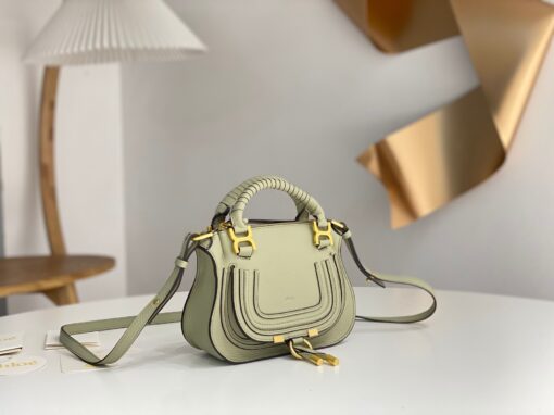CHLOÉ Marcie Mini Double Carry Bag: Elegance in Miniature. Introducing a charming, petite rendition of the iconic Marcie handbag, this mini double carry bag exudes elegance with its meticulous craftsmanship in grained calfskin. Its clean, sleek lines and gracefully contoured design elevate the relaxed, slouchy silhouette, while the hand-wrapped leather handles impart an artisanal touch. The addition of metallic buckles bestows a polished and refined finish to this exquisite creation. Equipped with both double handles and a long, detachable shoulder strap, this mini bag epitomizes versatility, making it a must-have accessory for any occasion.