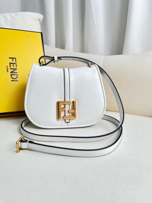 FENDI C’mon Mini. Embrace Elegance: Stefano Pilati's Curvaceous Creation. A petite satchel bag, graced with graceful, feminine curves, represents a masterpiece from the illustrious collection envisioned by the renowned Stefano Pilati. Fashioned from sumptuously smooth leather, this exquisite piece is adorned with meticulously embossed accents and edges, culminating in a striking FF logo proudly showcased on its elegant flap.