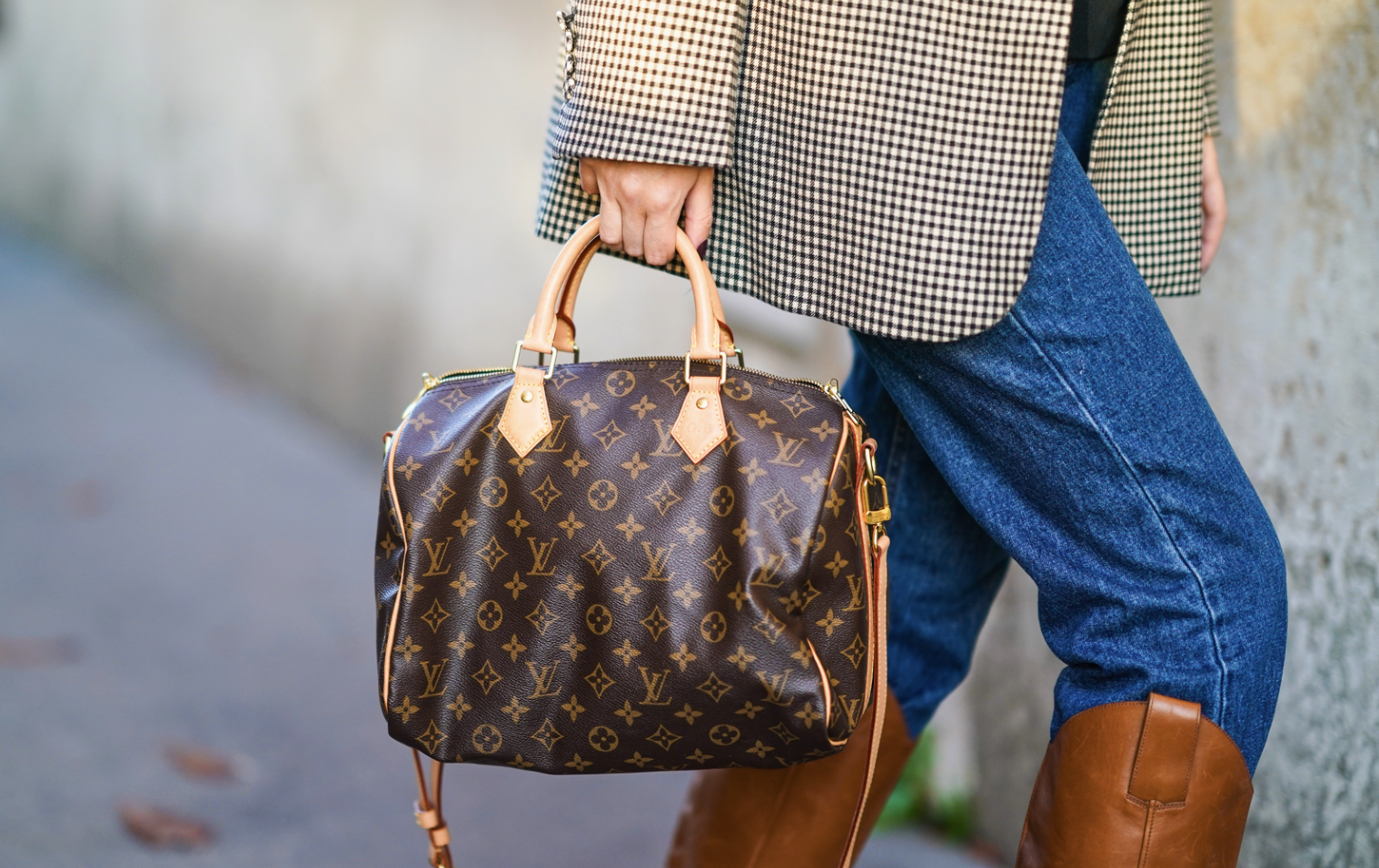 A woman carrying a LOUIS VUITTON Speedy bag while walking.