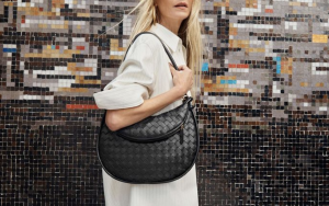A model elegantly holding a BOTTEGA VENETA bag in a modern urban setting.