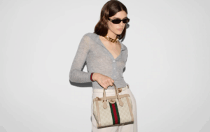 A confident woman struts with a white GUCCI Ophidia Small Tote With Web through the city.