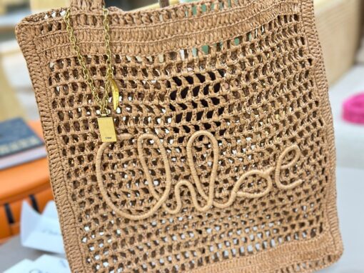 Summer Banana Tote Bag. Authentic quality luxury bag crafted in genuine leather comes with authenticity card, dust bag and gift bag. Heritage in Hand: Where Artisan Craft Meets Summer Elegance. Introducing the Summer Banana Tote—an artisanal masterpiece crafted from raffia and calfskin by a single artisan over 4.5 days in partnership with Made For A Woman. This spacious tote is adorned with a handwritten signature inspired by *loé’s rich heritage, while a playful dangling chain and delicate charms add the perfect finishing touch. A celebration of craftsmanship and effortless summer style.