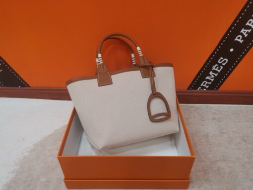 Steeple 25 Bag. Authentic quality luxury bag crafted in genuine leather comes with authenticity card, dust bag and gift bag. Where art meets heritage. The *rmès Steeple Bag is a charming fusion of heritage and artistry, crafted from a blend of canvas and Swift leather. Its design pays tribute to *rmès’ equestrian roots with whip-shaped handles and a stirrup-inspired charm, adding a playful yet sophisticated touch. Lightweight yet spacious, the Steeple is ideal for daily use. Whether you opt for a vibrant motif or a sleek, single-color design, this bag stands out as an artistic expression of luxury that seamlessly integrates into a modern lifestyle. Praised for its unique aesthetic and accessibility within the *rmès lineup, the Steeple Bag is adored by fashion enthusiasts who appreciate its colorful palette and bold personality. While it’s best suited for those who enjoy the texture and look of canvas, it remains a versatile statement piece that captures the spirit of everyday elegance.