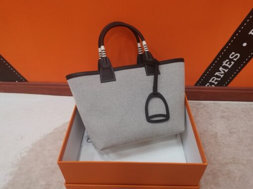 Steeple 25 Bag. Authentic quality luxury bag crafted in genuine leather comes with authenticity card, dust bag and gift bag. Where art meets heritage. The *rmès Steeple Bag is a charming fusion of heritage and artistry, crafted from a blend of canvas and Swift leather. Its design pays tribute to *rmès’ equestrian roots with whip-shaped handles and a stirrup-inspired charm, adding a playful yet sophisticated touch. Lightweight yet spacious, the Steeple is ideal for daily use. Whether you opt for a vibrant motif or a sleek, single-color design, this bag stands out as an artistic expression of luxury that seamlessly integrates into a modern lifestyle. Praised for its unique aesthetic and accessibility within the *rmès lineup, the Steeple Bag is adored by fashion enthusiasts who appreciate its colorful palette and bold personality. While it’s best suited for those who enjoy the texture and look of canvas, it remains a versatile statement piece that captures the spirit of everyday elegance.