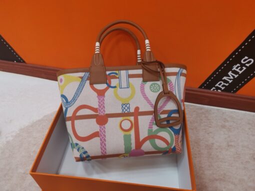 Steeple 25 Bag. Authentic quality luxury bag crafted in genuine leather comes with authenticity card, dust bag and gift bag. Where art meets heritage. The *rmès Steeple Bag is a charming fusion of heritage and artistry, crafted from a blend of canvas and Swift leather. Its design pays tribute to *rmès’ equestrian roots with whip-shaped handles and a stirrup-inspired charm, adding a playful yet sophisticated touch. Lightweight yet spacious, the Steeple is ideal for daily use. Whether you opt for a vibrant motif or a sleek, single-color design, this bag stands out as an artistic expression of luxury that seamlessly integrates into a modern lifestyle. Praised for its unique aesthetic and accessibility within the *rmès lineup, the Steeple Bag is adored by fashion enthusiasts who appreciate its colorful palette and bold personality. While it’s best suited for those who enjoy the texture and look of canvas, it remains a versatile statement piece that captures the spirit of everyday elegance.