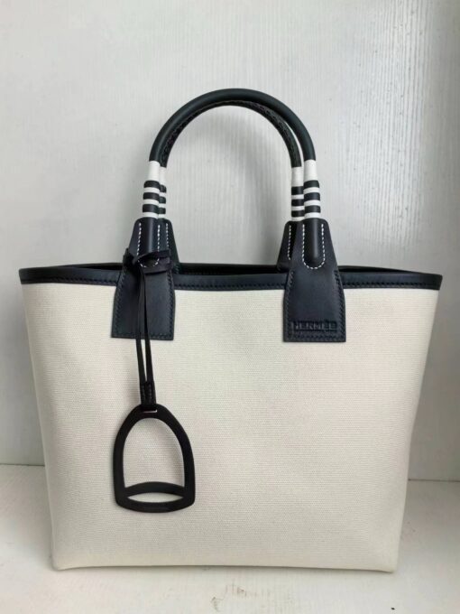 Steeple 25 Bag. Authentic quality luxury bag crafted in genuine leather comes with authenticity card, dust bag and gift bag. Where art meets heritage. The *rmès Steeple Bag is a charming fusion of heritage and artistry, crafted from a blend of canvas and Swift leather. Its design pays tribute to *rmès’ equestrian roots with whip-shaped handles and a stirrup-inspired charm, adding a playful yet sophisticated touch. Lightweight yet spacious, the Steeple is ideal for daily use. Whether you opt for a vibrant motif or a sleek, single-color design, this bag stands out as an artistic expression of luxury that seamlessly integrates into a modern lifestyle. Praised for its unique aesthetic and accessibility within the *rmès lineup, the Steeple Bag is adored by fashion enthusiasts who appreciate its colorful palette and bold personality. While it’s best suited for those who enjoy the texture and look of canvas, it remains a versatile statement piece that captures the spirit of everyday elegance.